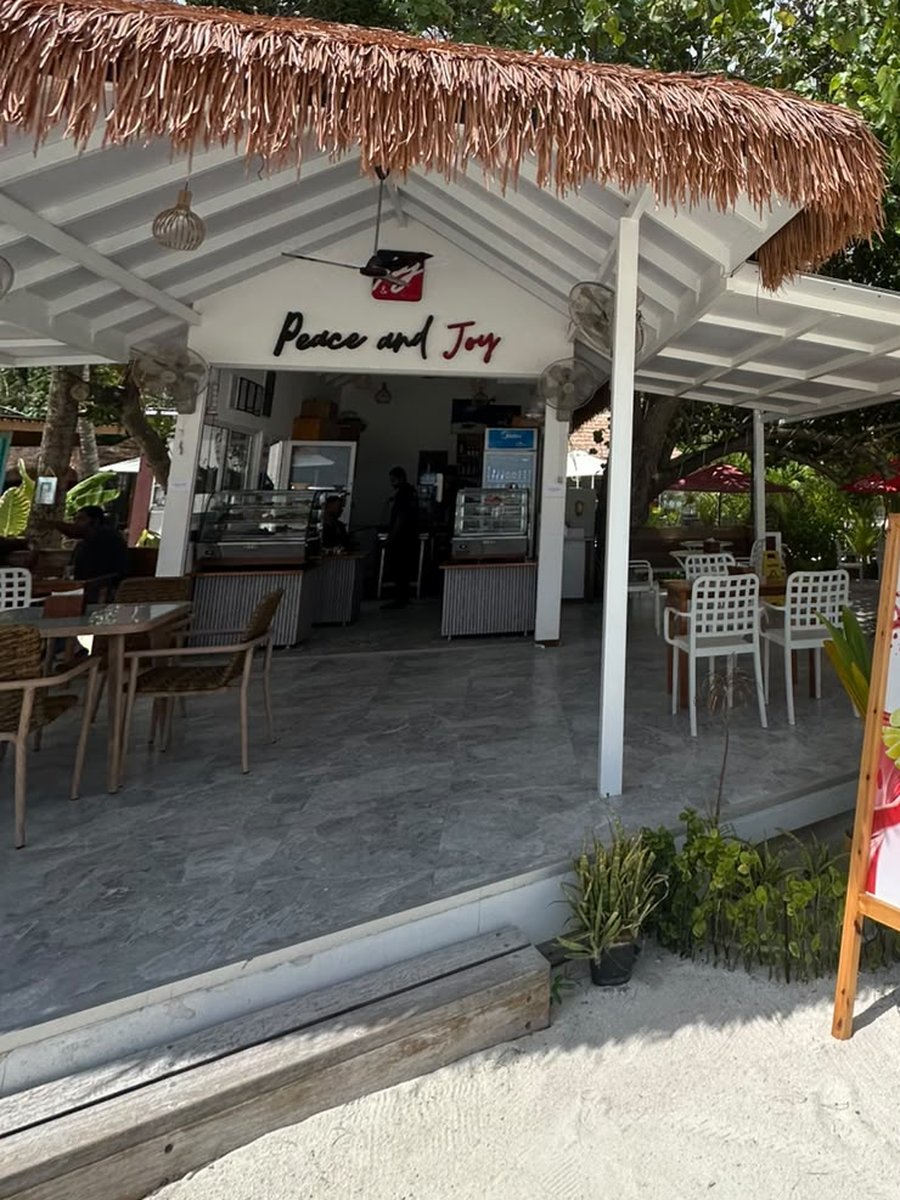 The cafe today, trading as Peace and Joy, with red signage, plastic chairs and umbrellas